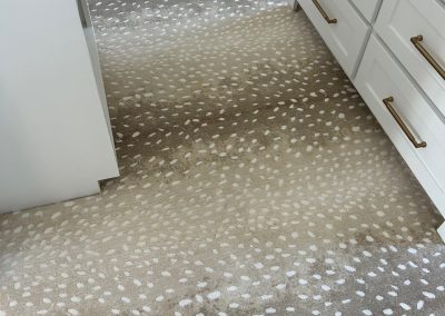 Beige carpet with white spots, resembling a deer pattern, next to white cabinets with gold handles—beautifully installed by Eastman’s Carpets Inc, your trusted choice for flooring services.