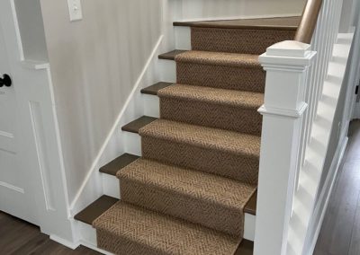 Carpeted stairs with a herringbone pattern runner by Eastman's Carpets and a white railing in a modern home with wood floors.