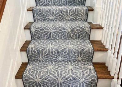 Stairs with a gray and white geometric-patterned carpet runner from Eastman's Carpets and wooden steps with white railings, showcasing expert flooring services.