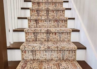 Patterned beige and brown carpet runner on wooden stairs with white railings on both sides—a stylish flooring solution that enhances any staircase.
