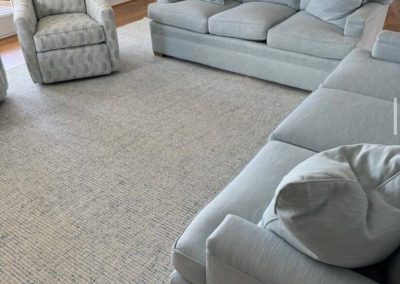 Light blue sofas and an armchair are arranged around a large textured area rug on stunning flooring by Eastman's Carpets Inc, brightening up the living room.