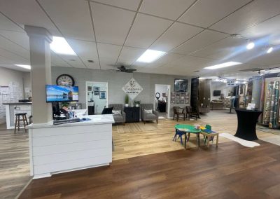 A flooring showroom offering expert flooring solutions, featuring a reception desk, seating area, kids’ table, and an array of flooring samples on display.