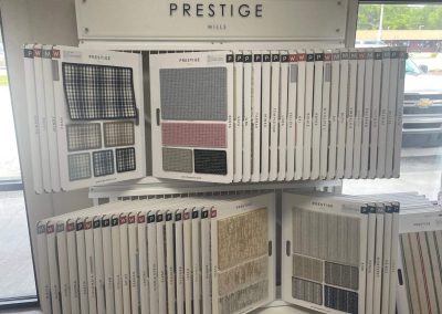Sample boards with various carpet swatches displayed on shelves under a sign that reads “Prestige Mills” at Eastman's Carpets Inc, known for quality flooring services and a wide selection to fit any style.