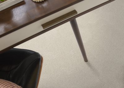 A wood desk with a drawer, black chair, and a glass of water on a light-colored carpet.