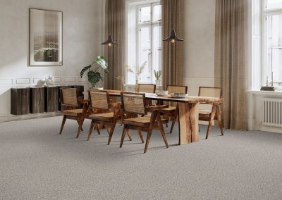 A dining room with a wooden table, six chairs, pendant lights, and large windows with beige curtains.